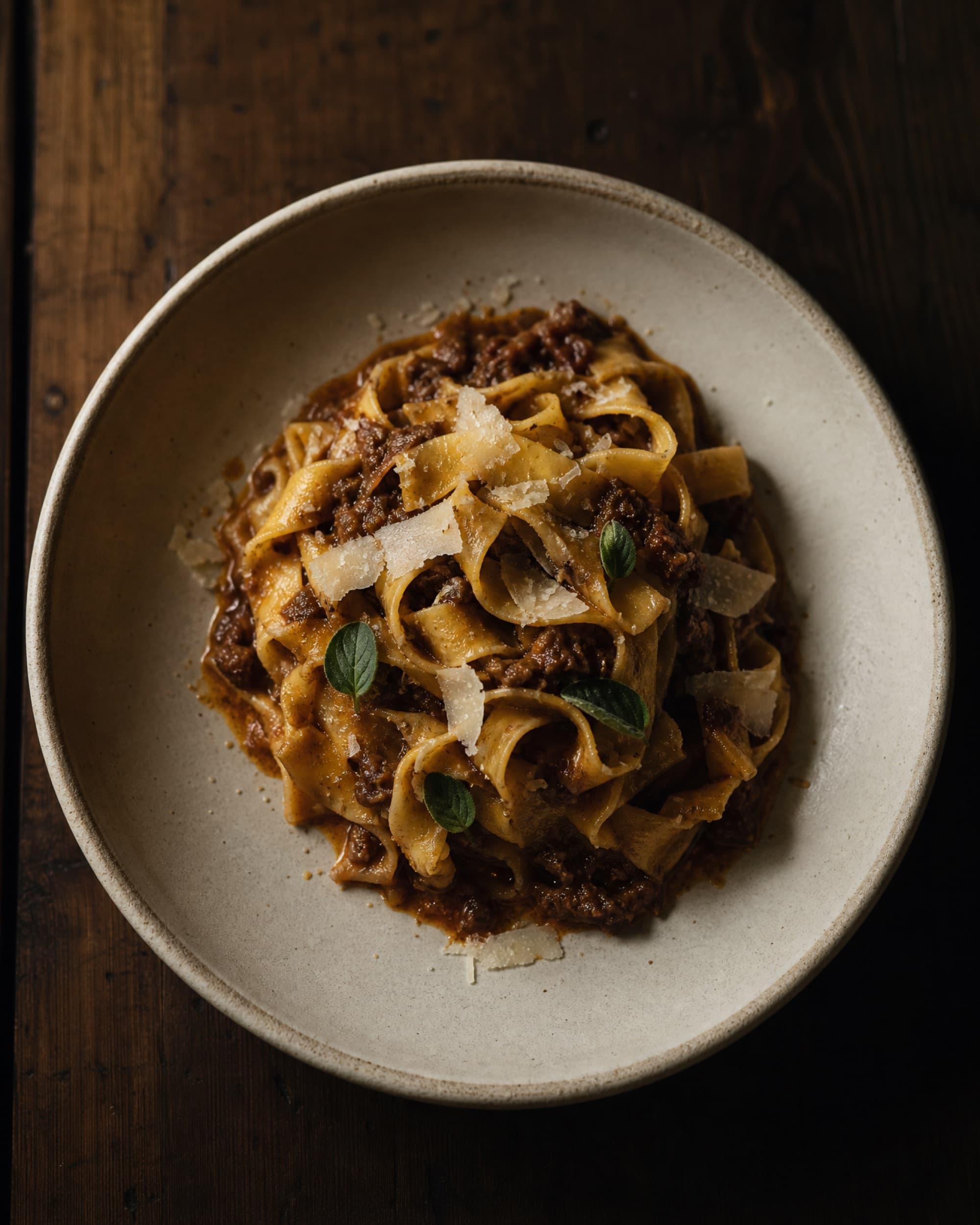 Hand cut tagliatelle in aged beef ragu with shaved pecorino, in a bone white bowl.